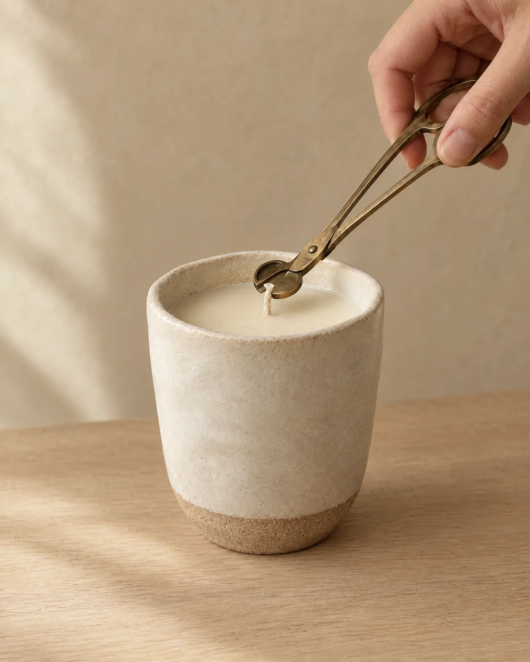 Trimming the wick of a beeswax candle in a stoneware cup