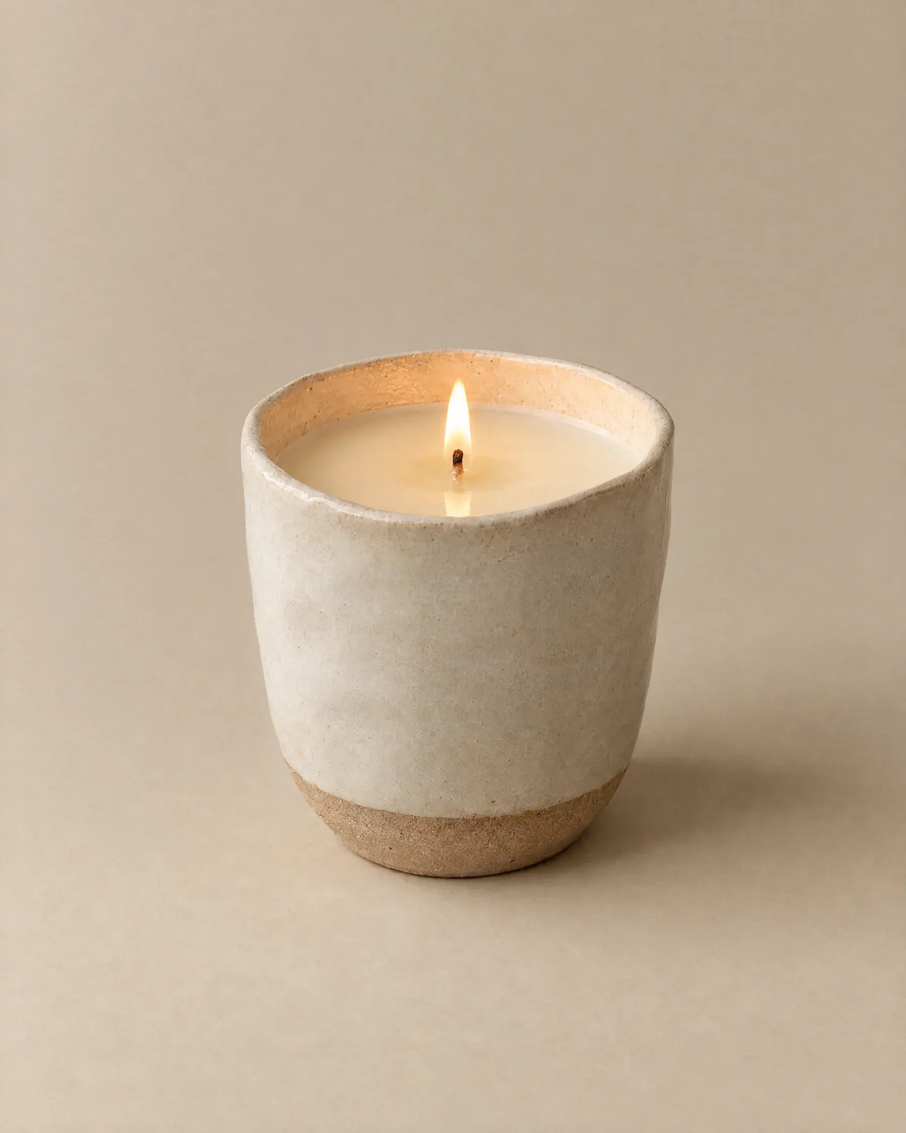A lit beeswax candle in a bone stoneware cup