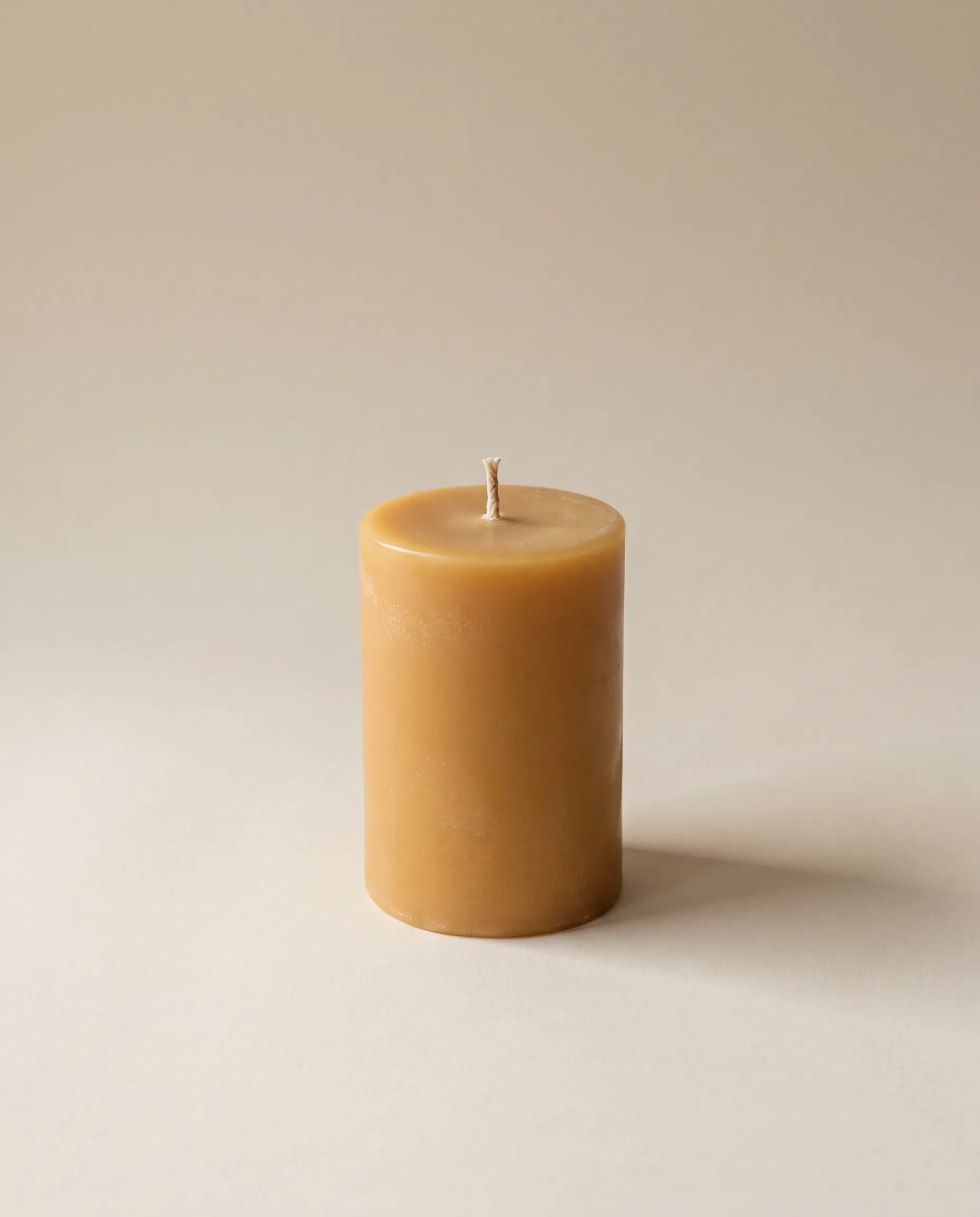 A short golden beeswax pillar candle with a cotton wick on a pale background