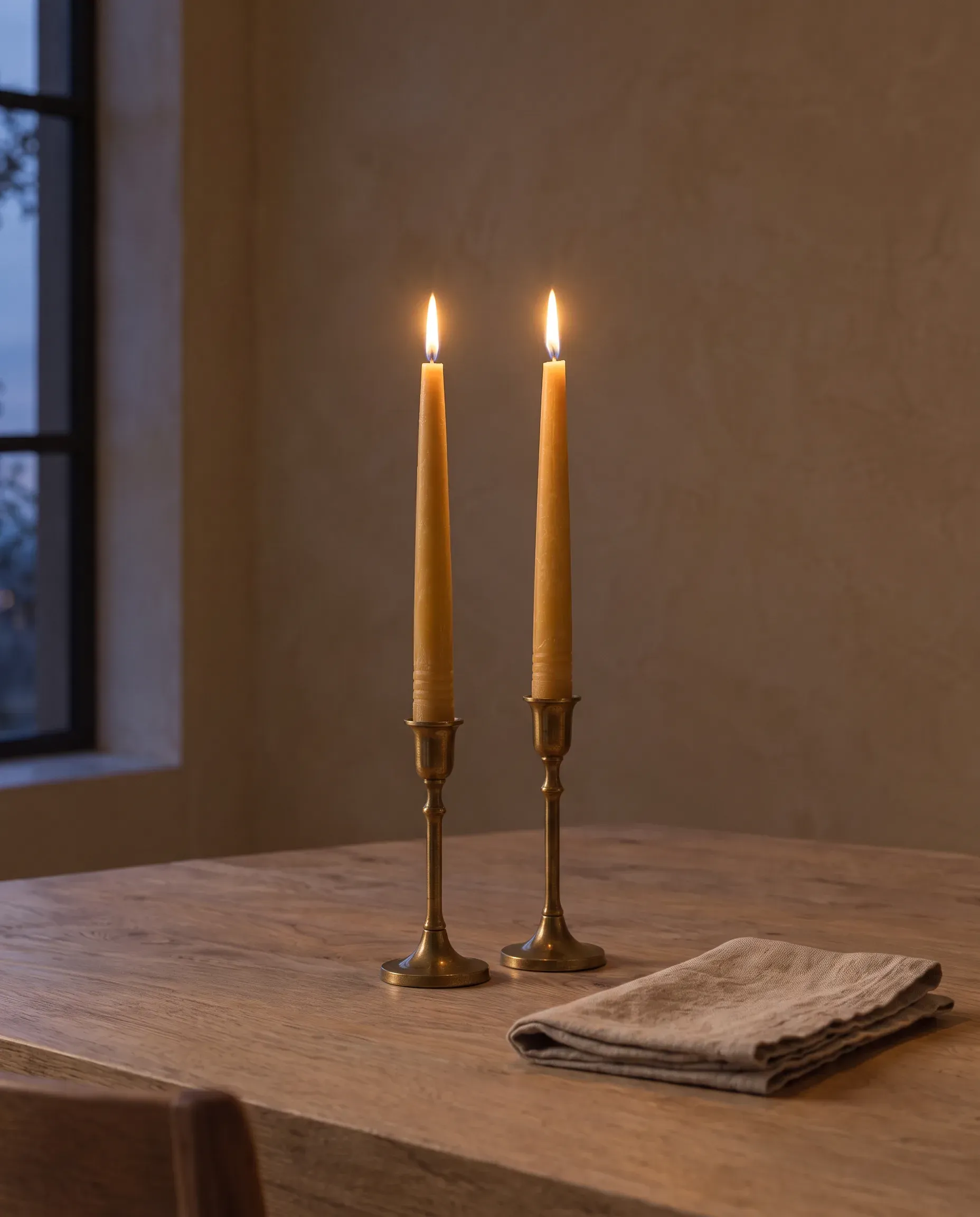 Two lit beeswax taper candles in brass candlesticks